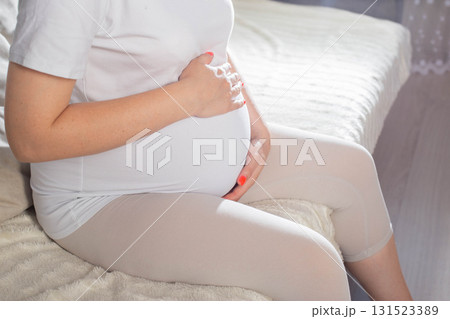 Pregnant woman relaxing at home in comfortable clothing while cradling her baby bump 131523389