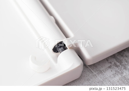 Broken hinge of a white toilet seat, close-up, low-quality plastic, industry 131523475
