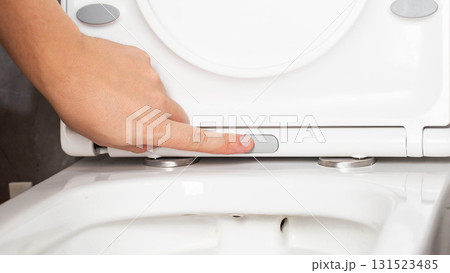 Close-up of finger pressing button on modern toilet seat cover to remove and disengage, close-up 131523485
