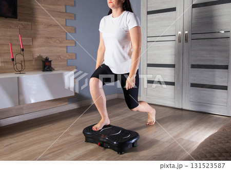 A young girl is doing sports on a vibration platform exercise machine at home in a home environment. The concept of getting rid of excess weight and cellulite. Sports device A young girl is doing sports on a vibration platform exercise machine at home in a home environment. The concept of getting rid of excess weight and cellulite. Sports device 131523587