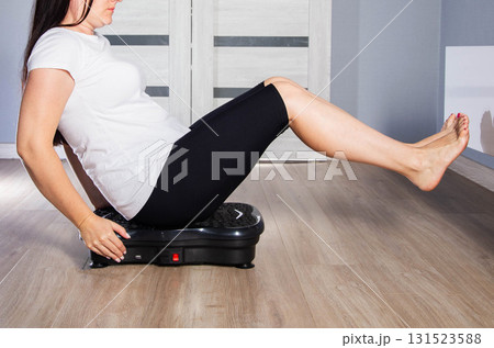 A young girl is doing sports on a vibration platform exercise machine at home in a home environment. The concept of getting rid of excess weight and cellulite. Sports device A young girl is doing sports on a vibration platform exercise machine at home in a home environment. The concept of getting rid of excess weight and cellulite. Sports device 131523588