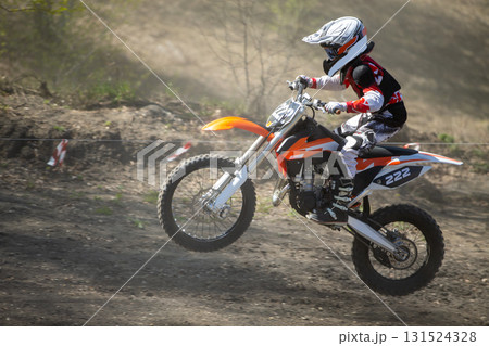 Junior motocross rider riding uphill on dusty track 131524328