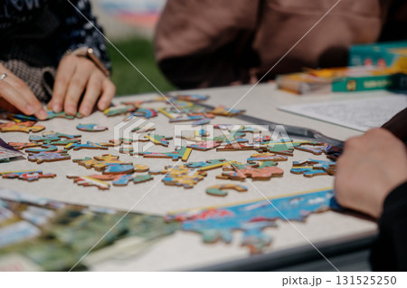 Several people are assembling a wooden puzzle in a park 131525250