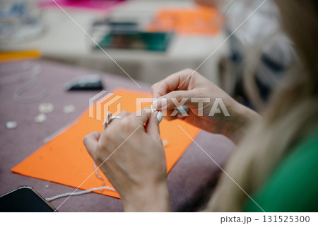 The hands of a master jeweler collect beads, a close-up of the jewelry making process 131525300