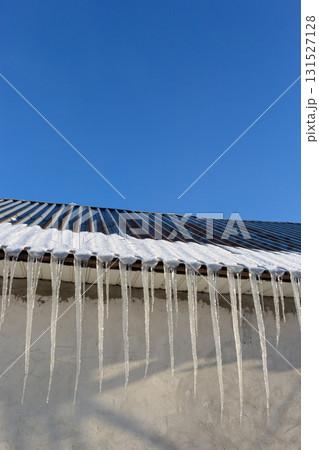 Sharp icicles and melted snow hanging from eaves of roof. Beautiful transparent icicles slowly gliding of a roof Sharp icicles and melted snow hanging from eaves of roof. Beautiful transparent icicles slowly gliding of a roof 131527128