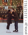A young couple in love kissing on an ice rink against the background of retro garlands with light bulbs and a Christmas tree in winter 131527811