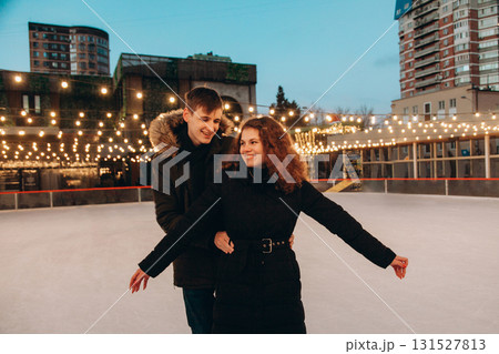 A young couple in love skating on a skating rink, arms apart, look at each other and smile A young couple in love skating on a skating rink, arms apart, look at each other and smile 131527813