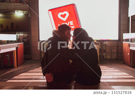 A young couple in love is sitting in a street cinema and looking at each other, hugging and kissing against the background of the screen 131527816