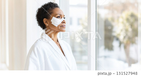 Elderly black woman with bandages on nose standing by window Elderly black woman with bandages on nose standing by window 131527948