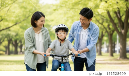 Asian parents teaching their young son how to ride a bicycle in the park. Happy family bonding and enjoying an outdoor activity together 131528499