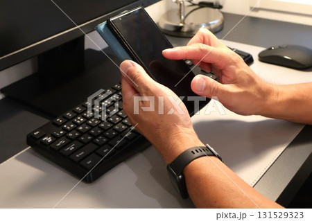 パソコン前でスマホを操作する男性の手元 パソコン前でスマホを操作する男性の手元 131529323