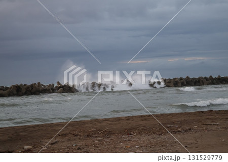 テトラポットの波除に白波が激しく当たる海と砂浜の海岸と雲と多い空の風景 テトラポットの波除に白波が激しく当たる海と砂浜の海岸と雲と多い空の風景 131529779