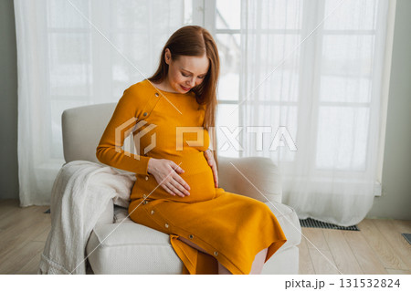 Pregnancy motherhood people expectation future. Pregnant woman with big belly sitting on chair near window at home. Girl hugging her tummy enjoying pregnancy. Maternity tenderness parenthood new life Pregnancy motherhood people expectation future. Pregnant woman with big belly sitting on chair near window at home. Girl hugging her tummy enjoying pregnancy. Maternity tenderness parenthood new life 131532824