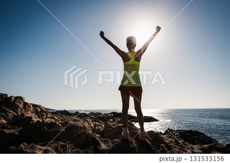 Athletic woman open arms to sunrise on seaside rocks Athletic woman open arms to sunrise on seaside rocks 131533156