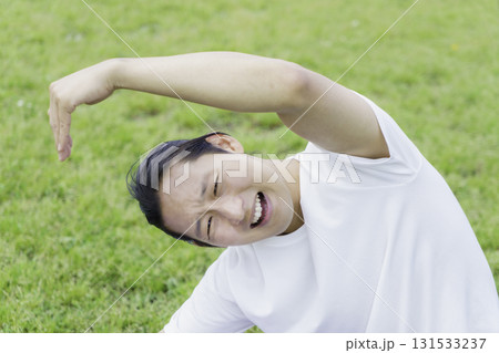 公園の芝生の上でストレッチをして苦しい顔をする若い男性 131533237