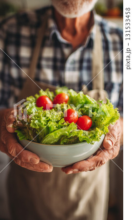 Elderly man holding fresh salad bowl with tomatoes in a rustic kitchen 131533458