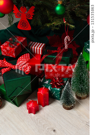 Traditional green and red gift boxes nestled beneath the Christmas tree, surrounded by glowing candles and festive decorations, creating a cozy and joyful holiday setting 131535863