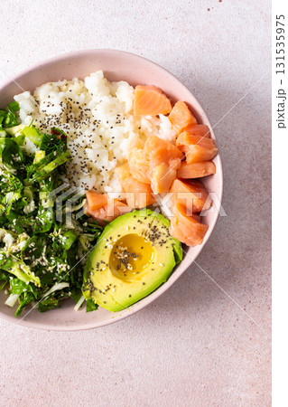 A nutritious breakfast bowl featuring rice, salmon, avocado, and fresh greens is presented beautifully in a bowl. Simple and healthy morning meal idea with vibrant colors 131535975