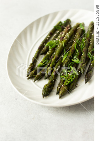 Steamed asparagus spears topped with fresh herbs are arranged neatly on a white plate. The dish appears vibrant and is suitable for a healthy meal or side Steamed asparagus spears topped with fresh herbs are arranged neatly on a white plate. The dish appears vibrant and is suitable for a healthy meal or side 131535999