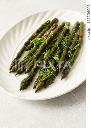 Steamed asparagus spears topped with fresh herbs are arranged neatly on a white plate. The dish appears vibrant and is suitable for a healthy meal or side 131536008