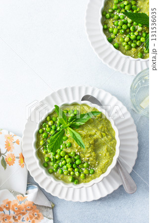 Bright green puree of green pea and broccoli fills a bowl, garnished with fresh mint and whole peas, showcasing a fresh and healthy soup perfect for lunch or dinner 131536035