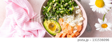 A colorful breakfast bowl features fresh salmon, creamy avocado slices, mixed greens, and herbs. Bright flowers add a cheerful touch to this morning meal setting, banner 131536096