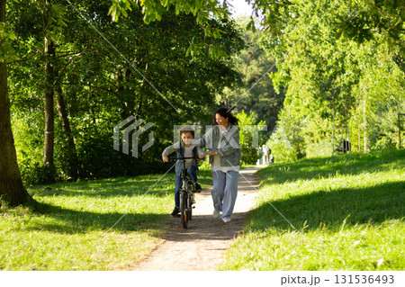 Caucasian millennial mother helping her son to ride bicycle in a park. Learning riding bike. 131536493