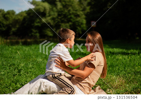Portrait of young Caucasian single mother hugging her cute small son outside in park sending time on summer day together. Motherhood concept. Portrait of young Caucasian single mother hugging her cute small son outside in park sending time on summer day together. Motherhood concept. 131536504