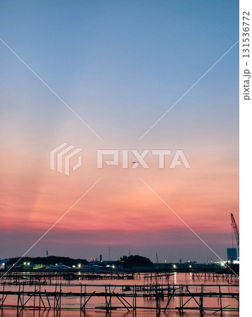Beautiful sunset over a coastal village with dramatic sun rays, calm waters, and traditional fishing structures. Perfect for travel, nature, and scenic themes. 131536772