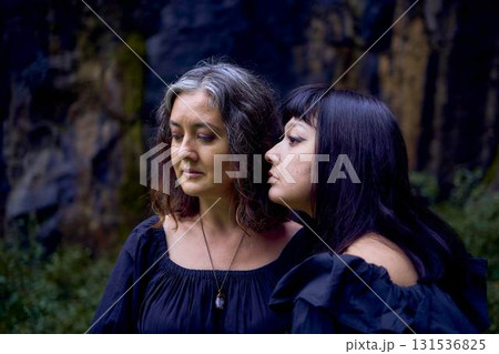 two women in the black long dresses sitting on black rocks on Halloween, performing a witch ritual, modern witch two women in the black long dresses sitting on black rocks on Halloween, performing a witch ritual, modern witch 131536825