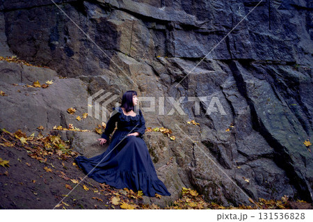 a woman in a black long dress sitting on black rocks on Halloween, modern witch a woman in a black long dress sitting on black rocks on Halloween, modern witch 131536828