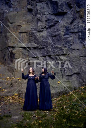 two women in the black long dresses near black rocks on Halloween holding a burning candle, performing a witch ritual, modern witch two women in the black long dresses near black rocks on Halloween holding a burning candle, performing a witch ritual, modern witch 131536849