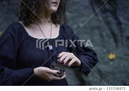 a woman in a black long dress near black rocks on Halloween holding a purple black crystal, performing a witch ritual, modern witch 131536872