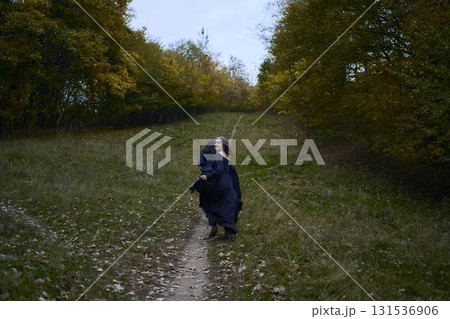 Two women in the long black dresses perform a historical reenactment of the Edwardian era dancing lovers on a hill near a majestic oak tree for Halloween. 131536906