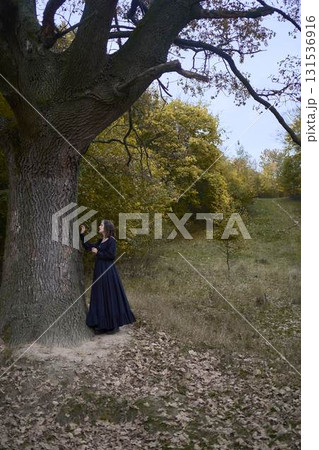 a women in the long black dresses perform a historical reenactment of the Edwardian era on a hill near a majestic oak tree for Halloween. 131536916