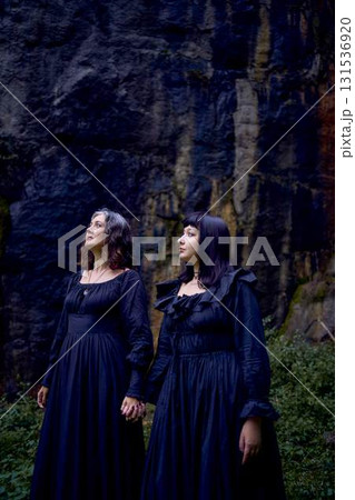 two women in the black long dresses sitting on black rocks on Halloween, performing a witch ritual, modern witch two women in the black long dresses sitting on black rocks on Halloween, performing a witch ritual, modern witch 131536920