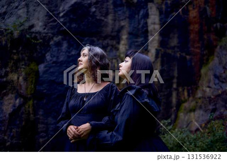 two women in the black long dresses sitting on black rocks on Halloween, performing a witch ritual, modern witch 131536922