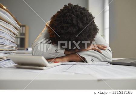 African American woman lays head on working desk, exhausted by lots of paperwork African American woman lays head on working desk, exhausted by lots of paperwork 131537169