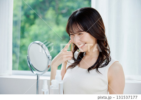 鏡で肌の状態を確認する笑顔の女性 131537177