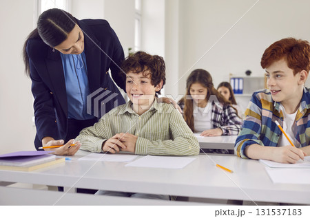 Young schoolboy answering on lesson sitting at the desk to a friendly teacher in the classroom. Young schoolboy answering on lesson sitting at the desk to a friendly teacher in the classroom. 131537183