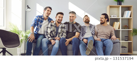 Happy male best friends sitting on couch together Happy male best friends sitting on couch together 131537194