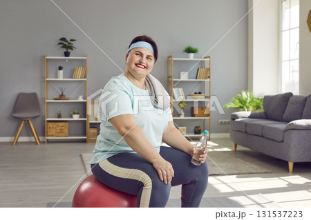 Fat woman wearing sportswear sitting on fit ball with a bottle of water after fit exercises at home Fat woman wearing sportswear sitting on fit ball with a bottle of water after fit exercises at home 131537223