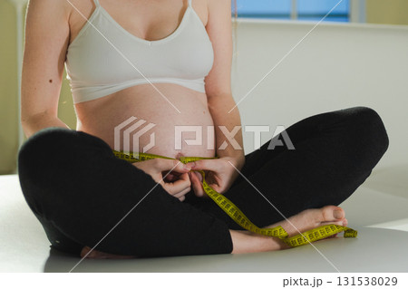 Pregnancy motherhood. Pregnant woman measuring big belly. Girl measuring her belly with tape to keep track of her fetus development. Woman enjoying pregnancy. Maternity tenderness parenthood new life Pregnancy motherhood. Pregnant woman measuring big belly. Girl measuring her belly with tape to keep track of her fetus development. Woman enjoying pregnancy. Maternity tenderness parenthood new life 131538029