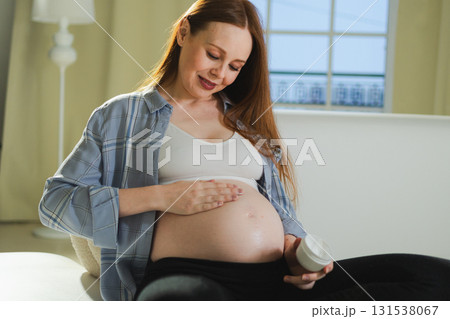 Pregnancy motherhood. Pregnant woman applying cream lotion on big belly takes care of her skin. Cosmetic product for prevention stretch mark. Girl enjoying pregnancy at home. Maternity health concept Pregnancy motherhood. Pregnant woman applying cream lotion on big belly takes care of her skin. Cosmetic product for prevention stretch mark. Girl enjoying pregnancy at home. Maternity health concept 131538067