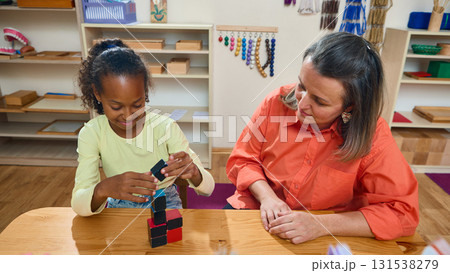 Child stacking educational cubes under psychologist supervision 131538279
