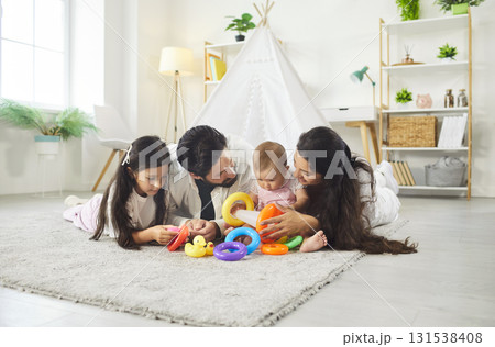 Happy family playing together with rainbow rings of pyramid on carpet of living room at home 131538408