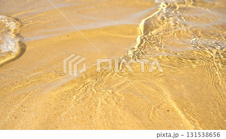 Close-up of transparent golden water with gentle ripples and sunlight reflections on a sandy beach surface du daytime, creating calming and peaceful atmosphere 131538656