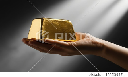Hand holding a heavy solid gold ingot against a dark blurred background emphasizing richness Hand holding a heavy solid gold ingot against a dark blurred background emphasizing richness 131539374