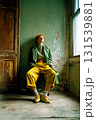 A woman in a green coat and yellow pants is sitting in front of a wall 131539881
