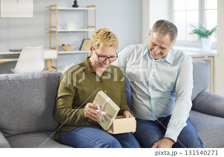 Happy senior couple sitting on sofa at home with present gift box celebrating holiday. 131540271